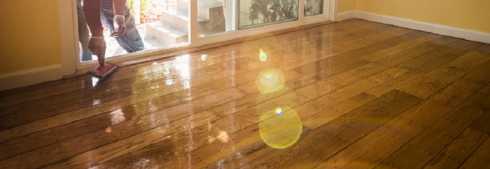 Person trägt Lack auf einen Holzboden auf